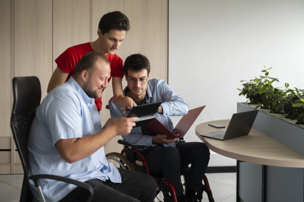 A group of colleagues discussing a project, with one holding a tablet and another reviewing a folder, symbolizing teamwork and collaboration in business management.